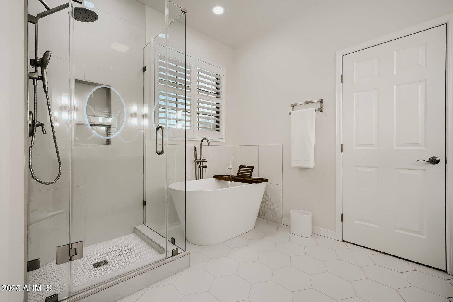 White bathroom with a glass shower, freestanding tub, and large hexagonal floor tiles.