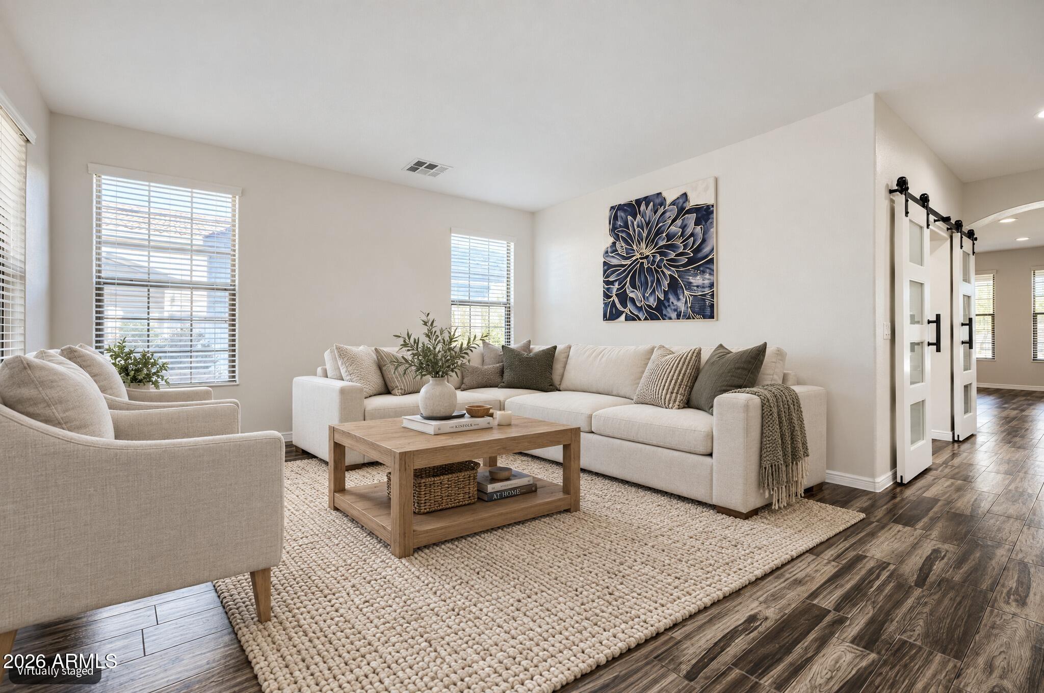 Virtually staged living room with a cream sectional, wood coffee table, textured rug, and white sliding barn doors.