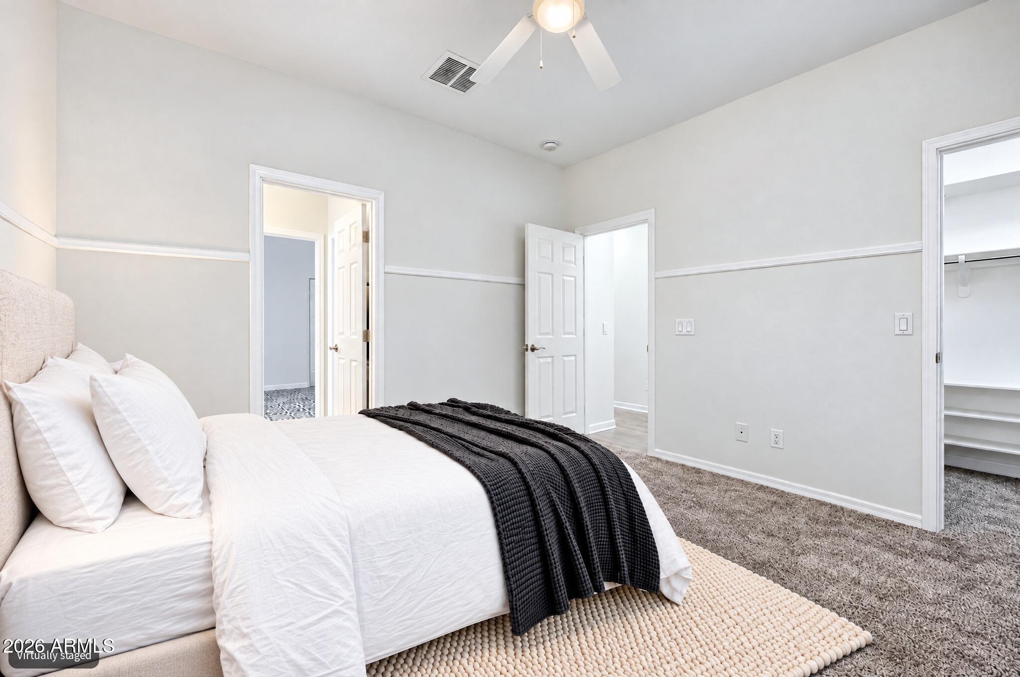 Virtually staged bedroom with a white bed and dark throw beside an open closet.