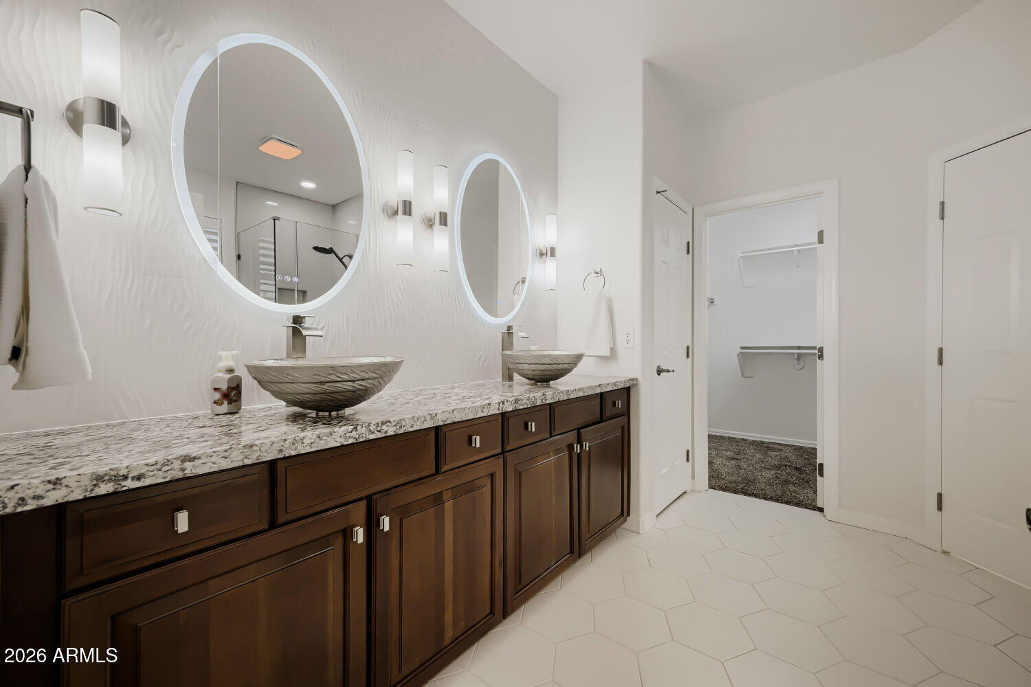 Bathroom with a dark double vanity, vessel sinks, and illuminated oval mirrors.