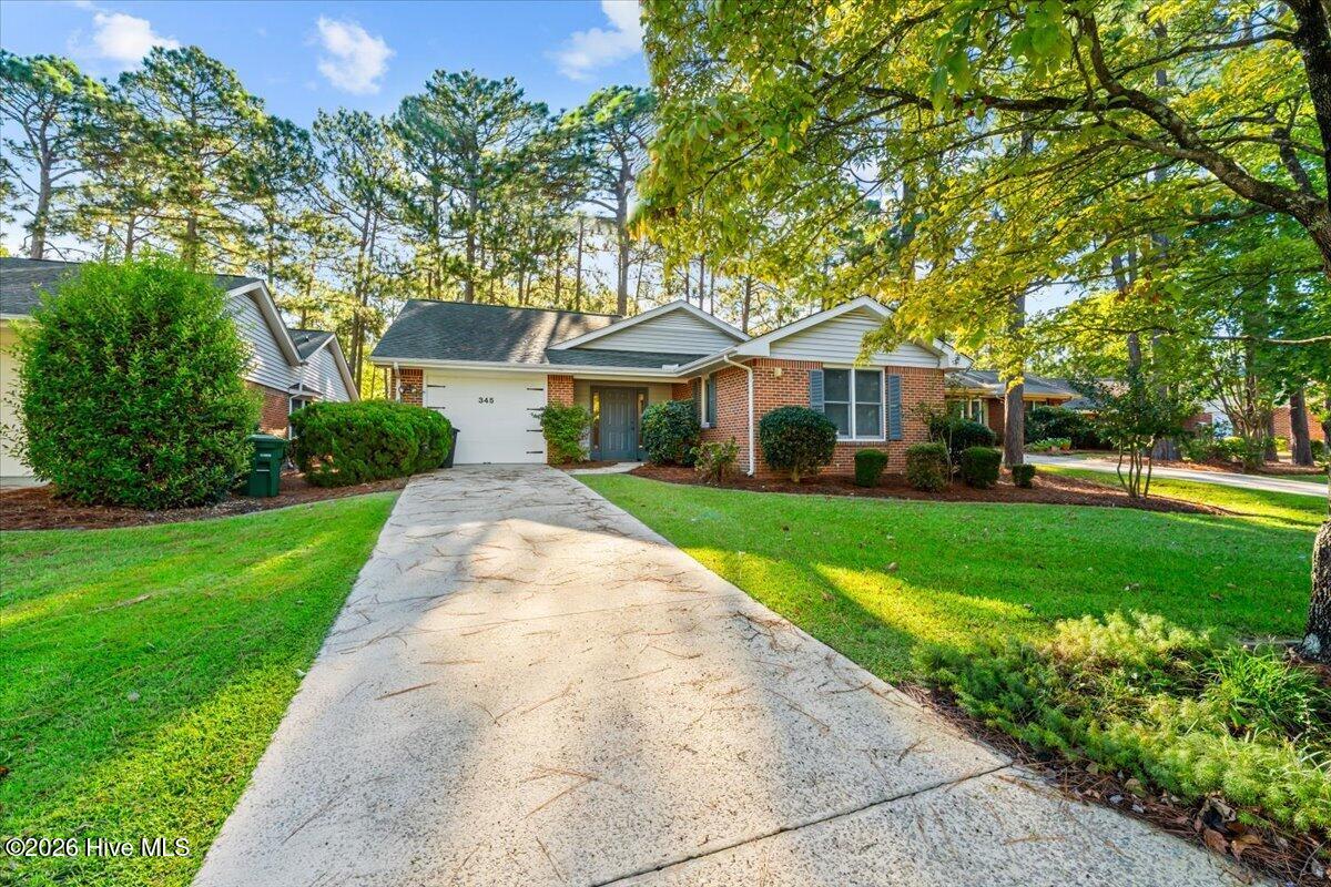 Brick ranch home with a white garage and a long concrete driveway beneath mature trees.