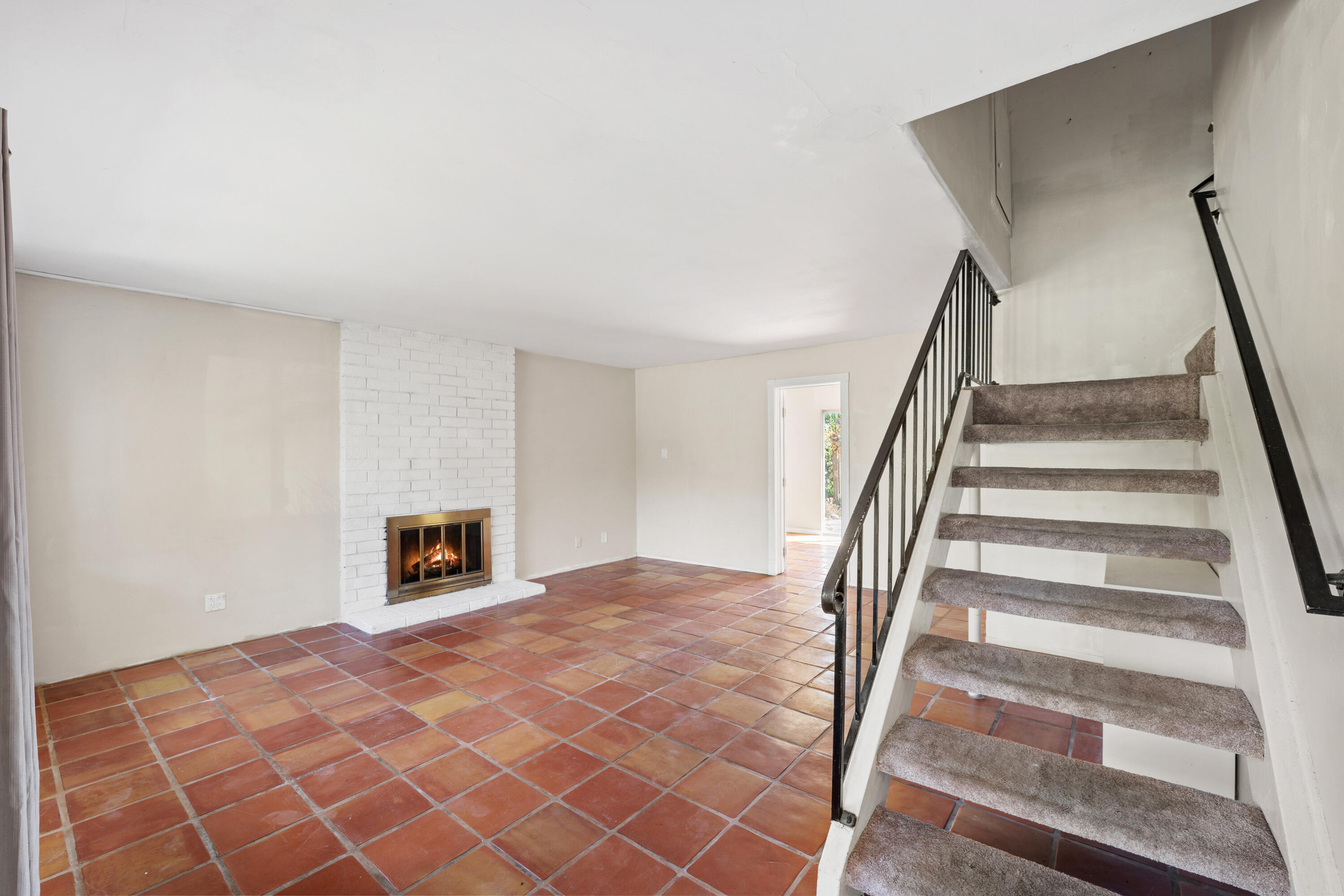 Unfurnished living room with terracotta tile, a brick fireplace, and carpeted stairs.