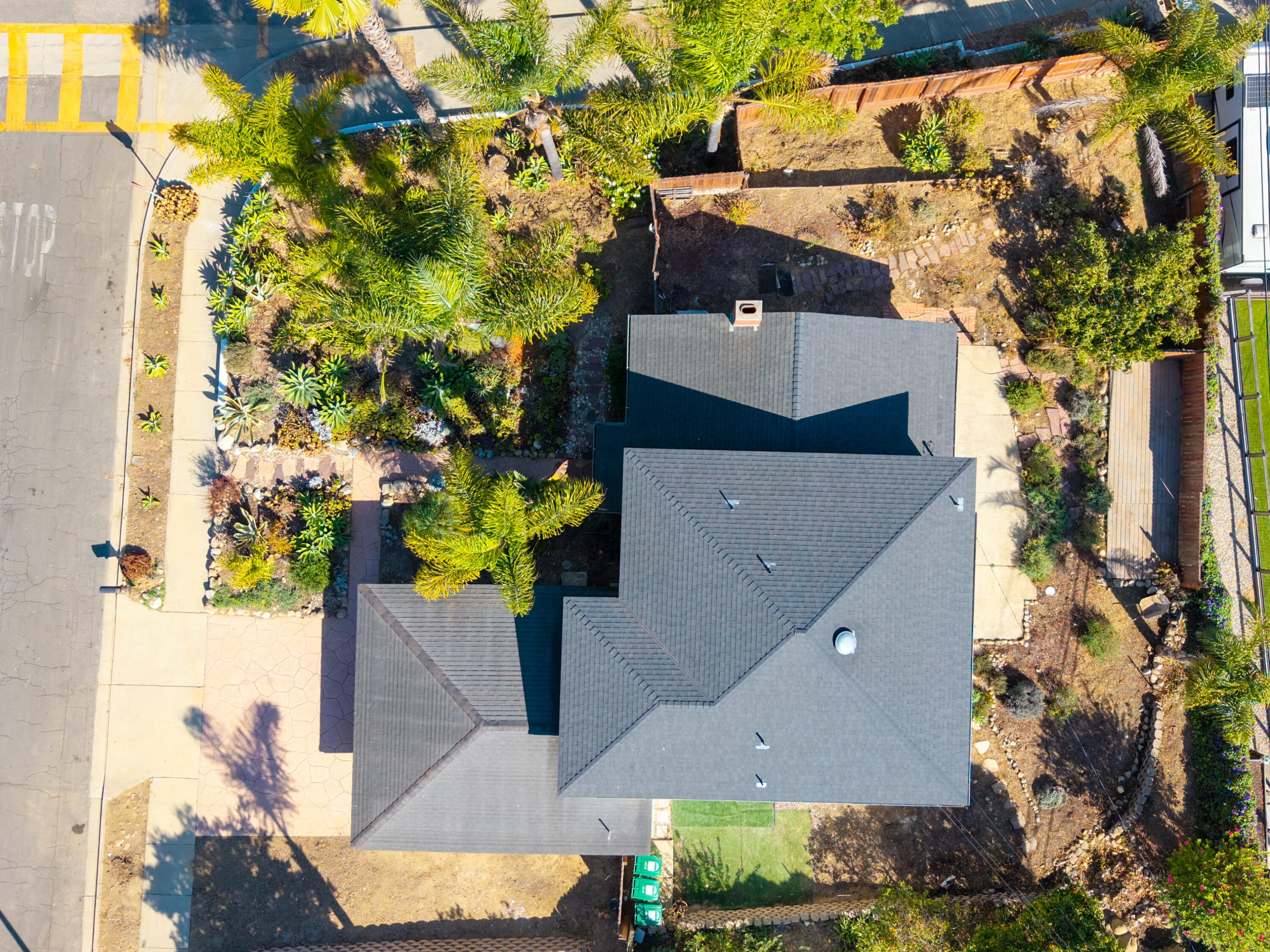 Aerial view of a home with a large gray roof and palm-filled landscaping.