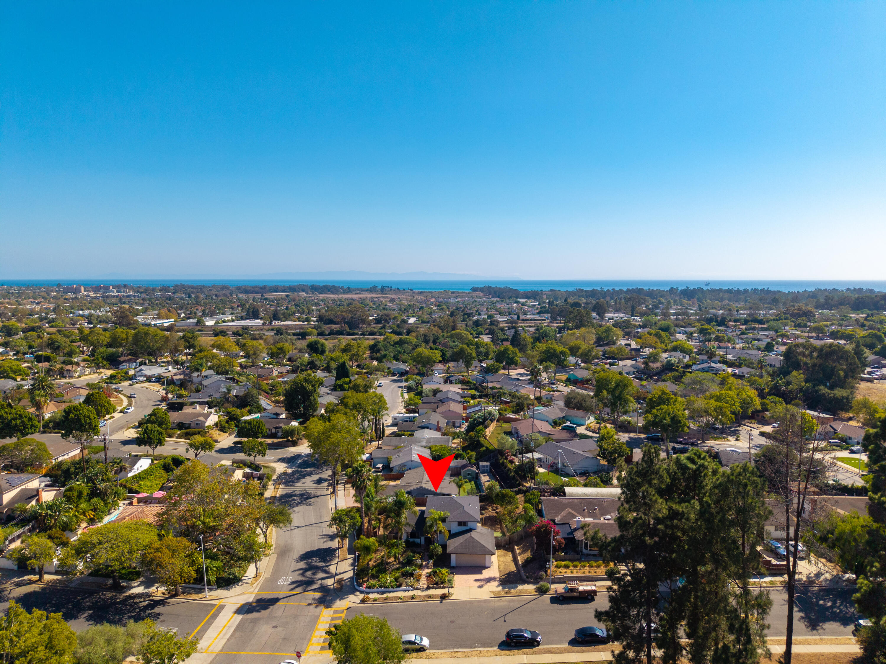Aerial view of a leafy neighborhood and ocean, with a red marker above the property.