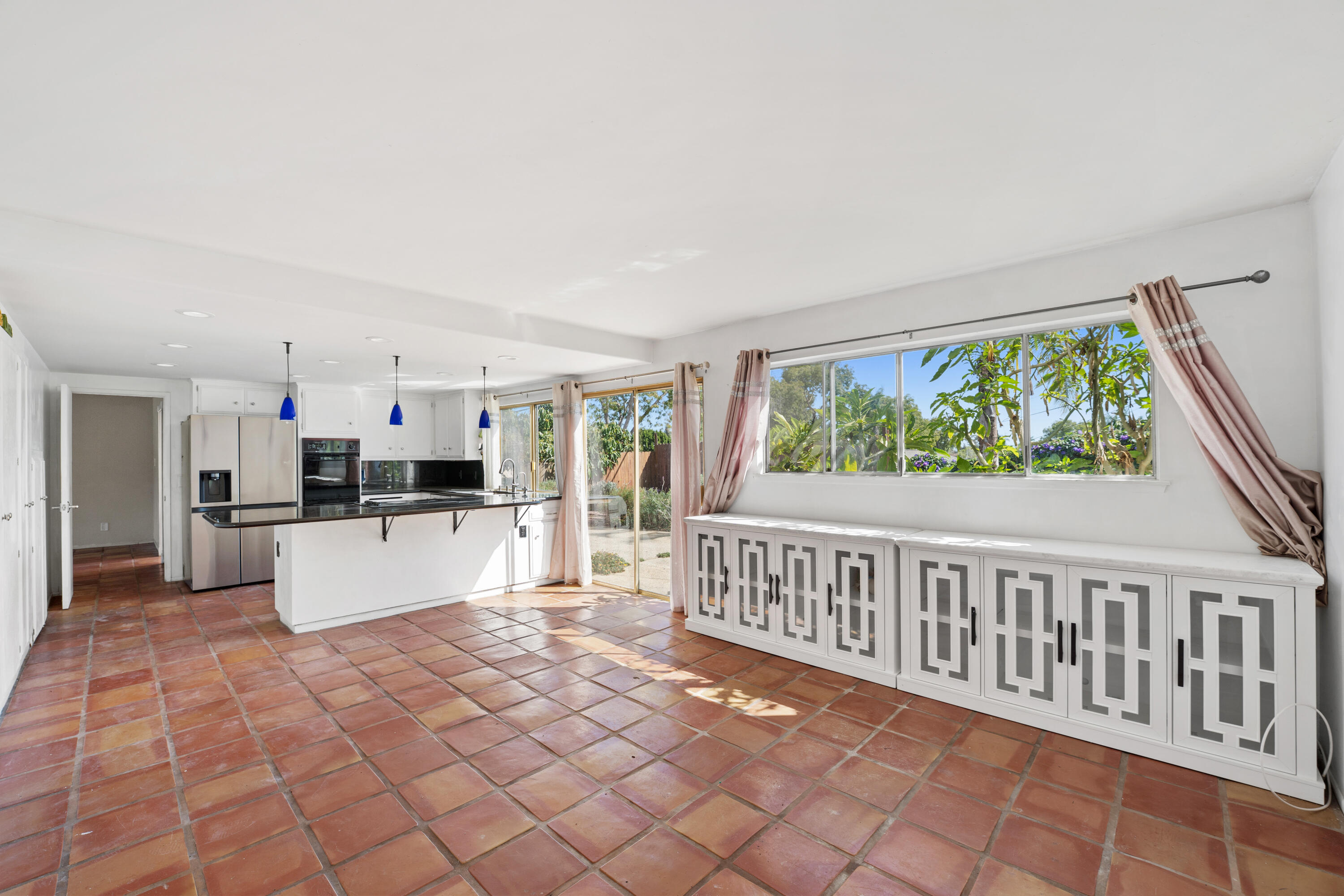 Open kitchen with terracotta tile floors, white cabinets, and large windows overlooking greenery.