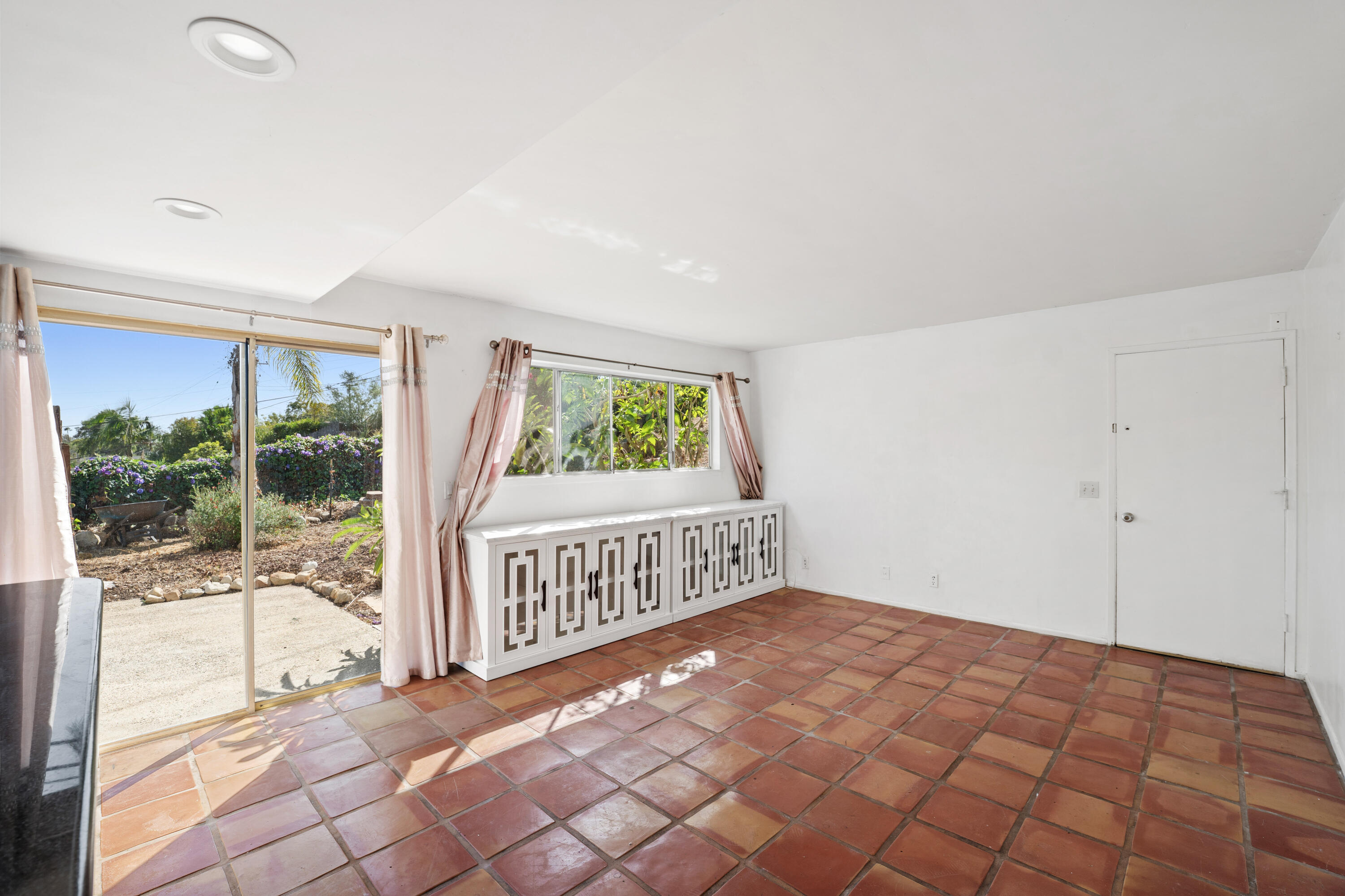 Bright room with terracotta tile floors, built-in cabinetry, and sliding glass doors overlooking a garden.