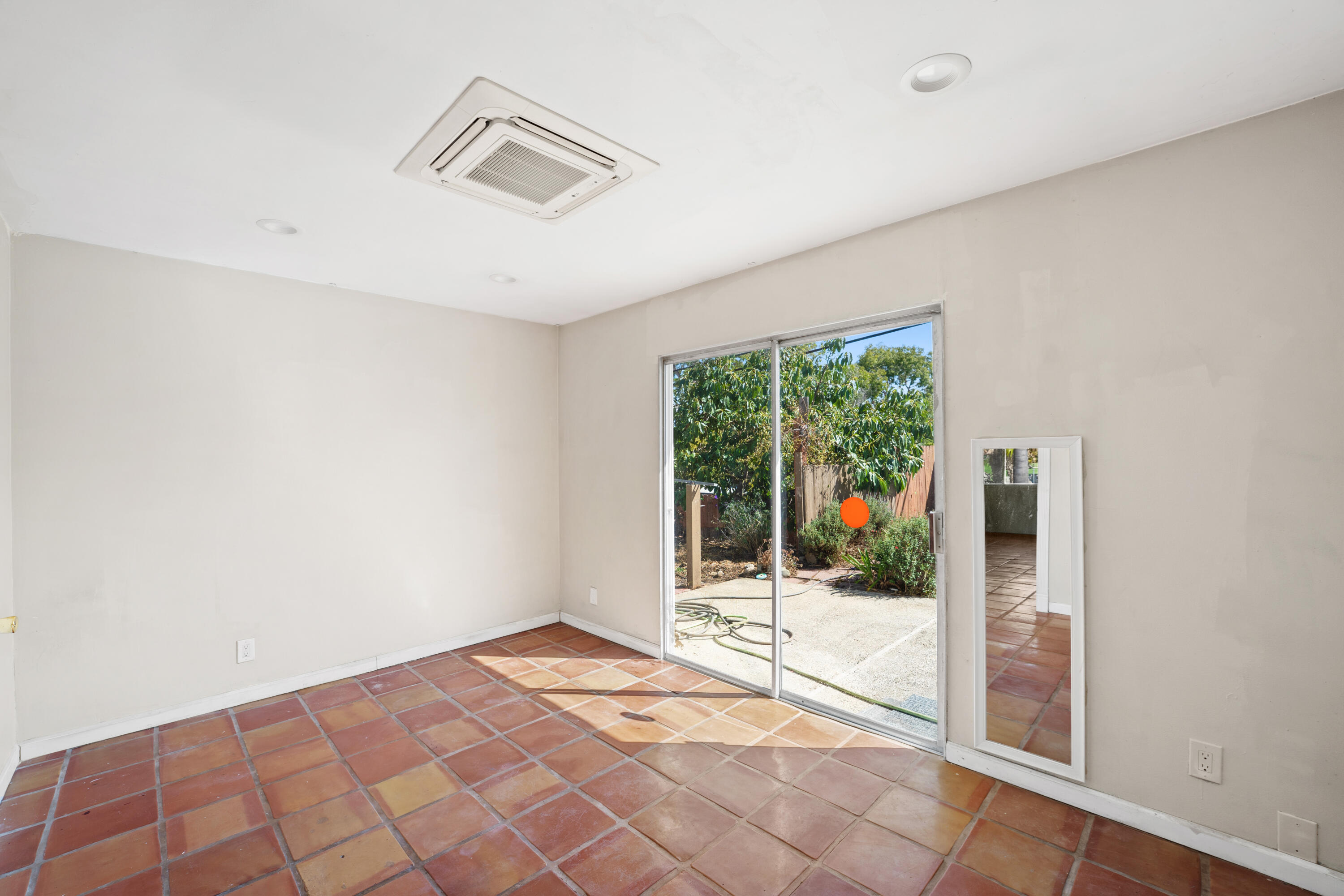 Empty tiled room with sliding glass doors opening onto a leafy patio.