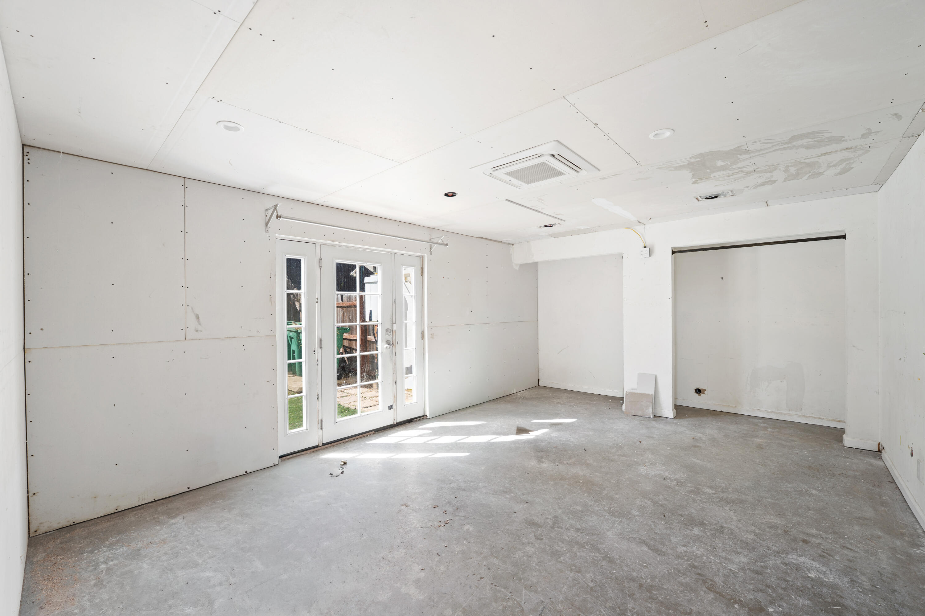 Unfinished garage with a concrete floor, French doors, and a ceiling-mounted air-conditioning unit.