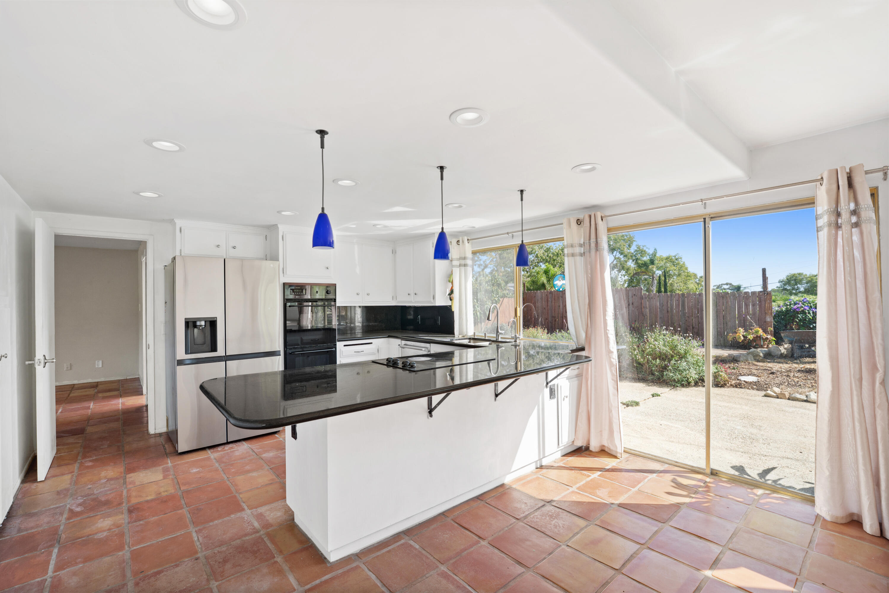 Kitchen with black island, terracotta tile floors, and sliding glass doors to a fenced yard.