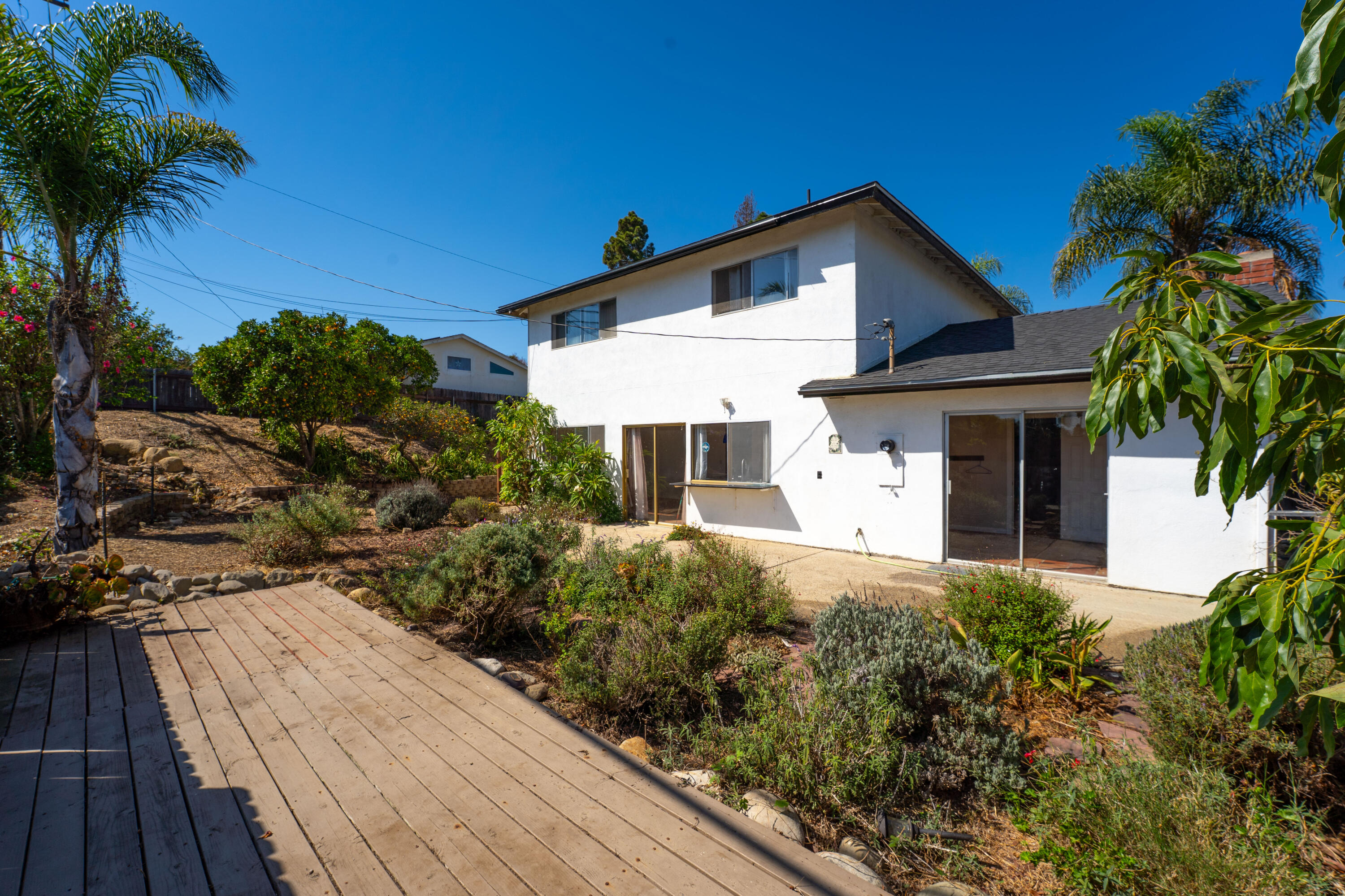 Two-story white house viewed from the rear, with a wooden deck and landscaped sloping yard.