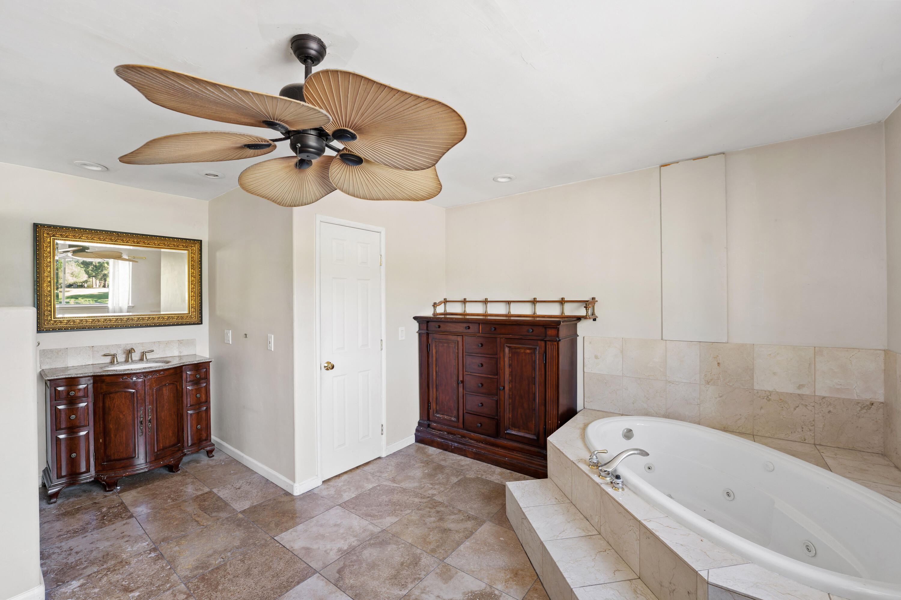 Bathroom with a tiled jetted soaking tub, dark wood vanity, and distinctive wood-blade ceiling fan.