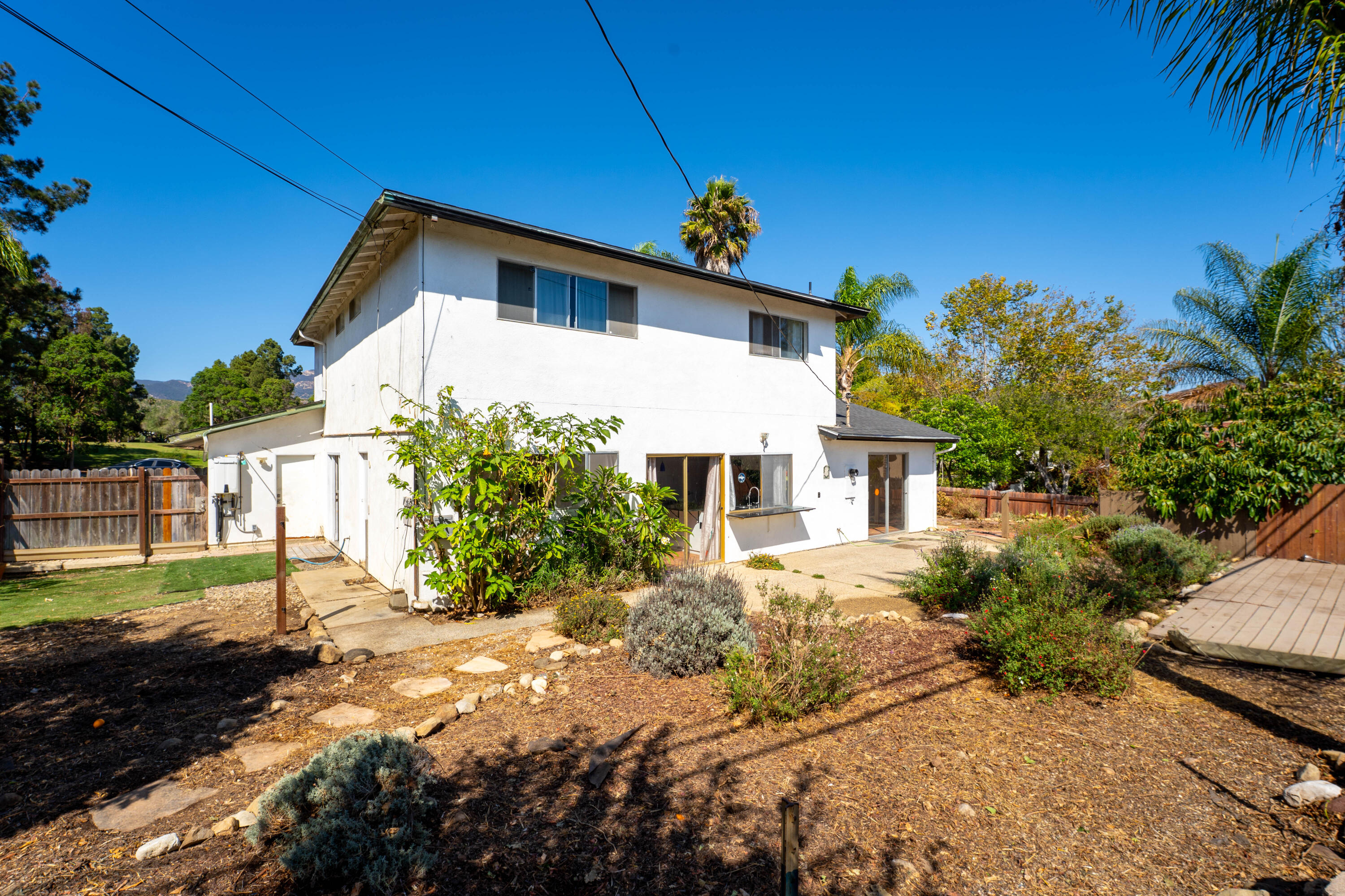 Rear of a two-story white house with a patio, landscaped yard, and wooden fencing.