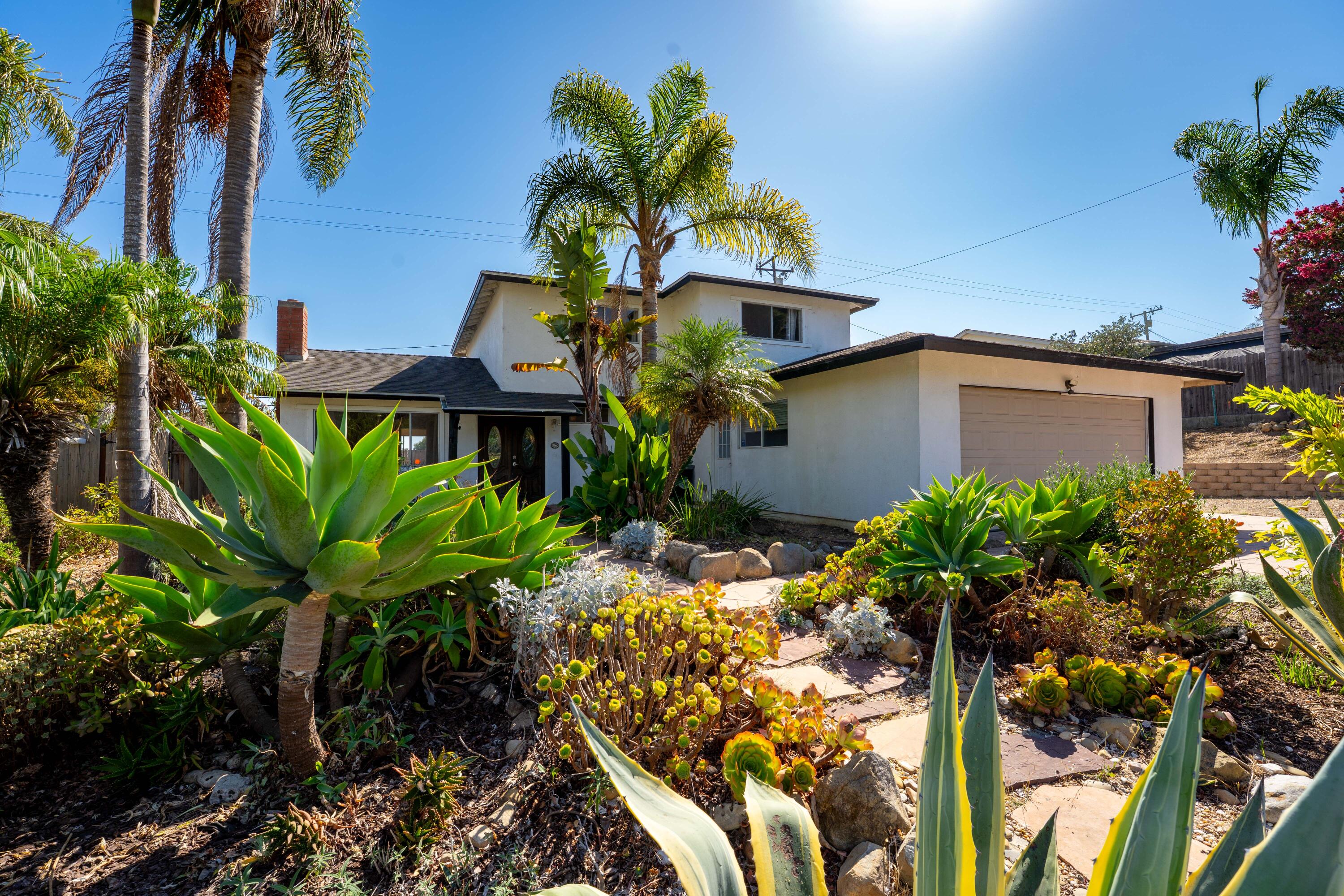 White two-story home with an attached garage behind palms and a garden of agave and succulents.