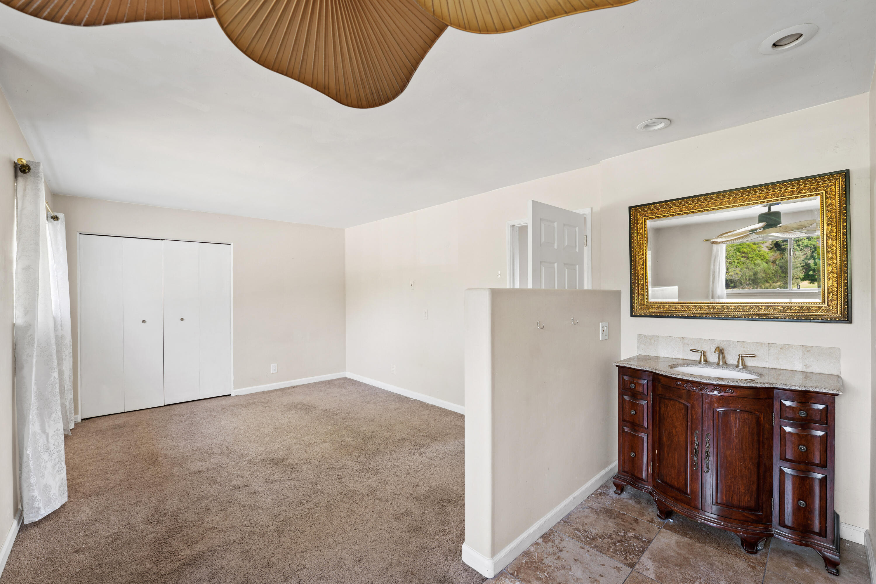 Carpeted bedroom with sliding closet doors and an adjoining dark wood vanity beneath an ornate mirror.