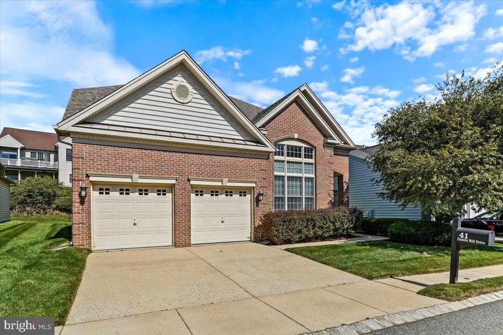 Red-brick house with two white garage doors, an arched window, and a concrete driveway.