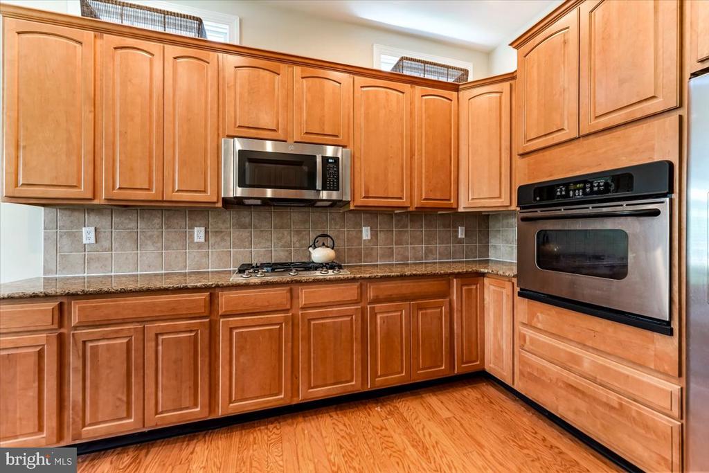 Kitchen with warm wood cabinetry, granite counters, stainless appliances, and hardwood flooring.