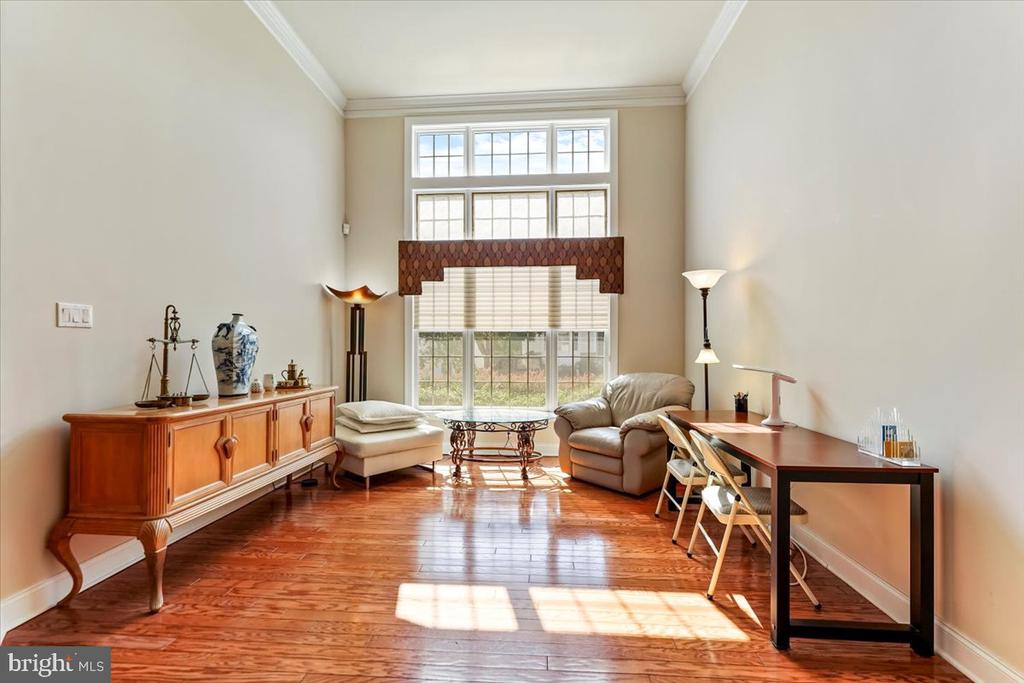 Furnished sitting room with polished hardwood floors, a desk, and tall windows with blinds.