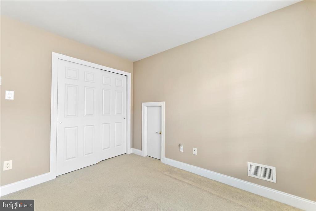 Empty carpeted room with large white closet doors and a small door.