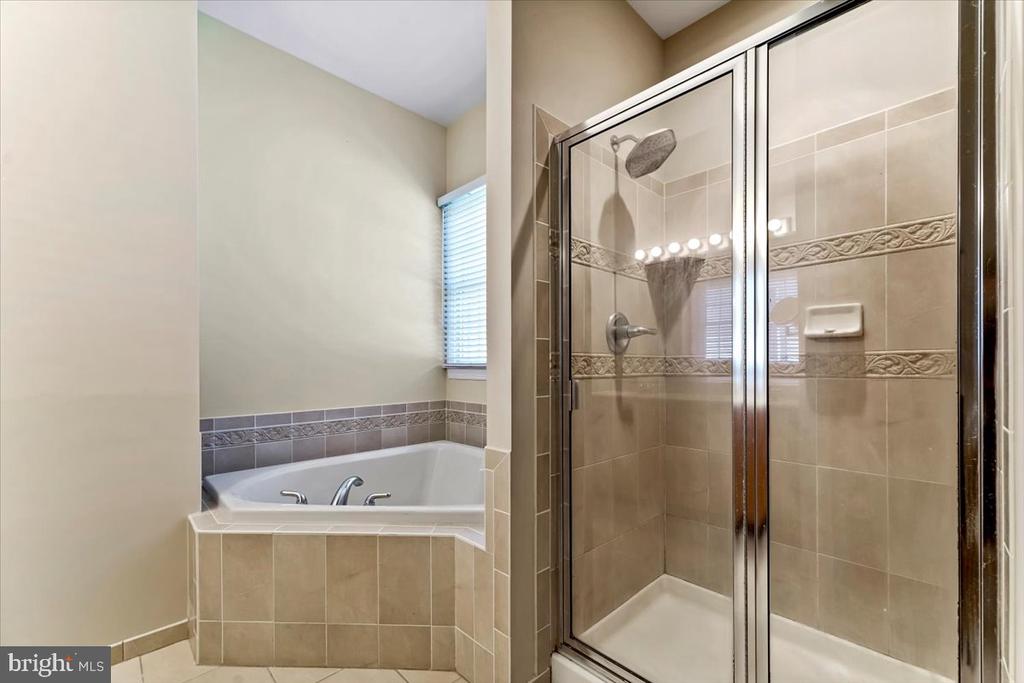 Bathroom with a corner soaking tub beneath a window and a separate glass-enclosed shower.
