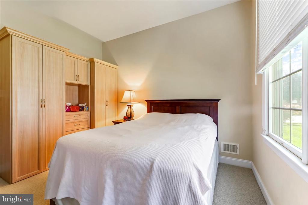 Bedroom with built-in light wood wardrobes, a large bed, and a tall window with white blinds.