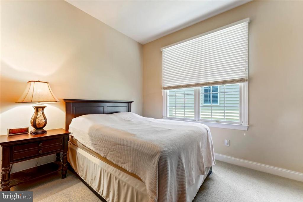 Bedroom with a dark wood headboard, bedside lamp, and wide window with white blinds.