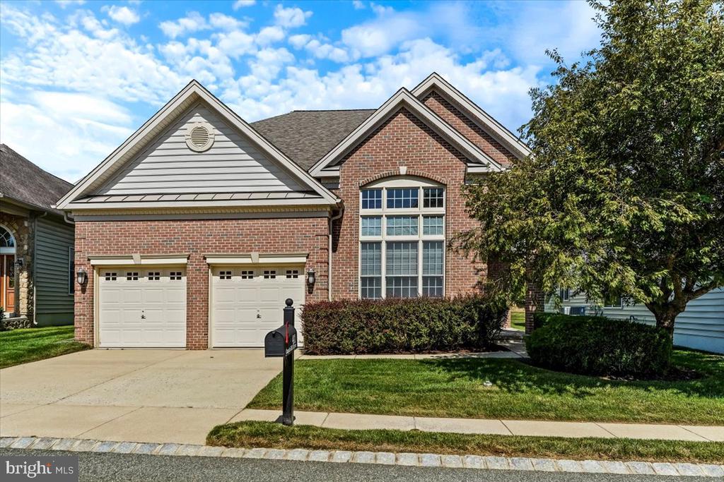 Brick home with a two-car garage, large front window, and mature tree beside the lawn.