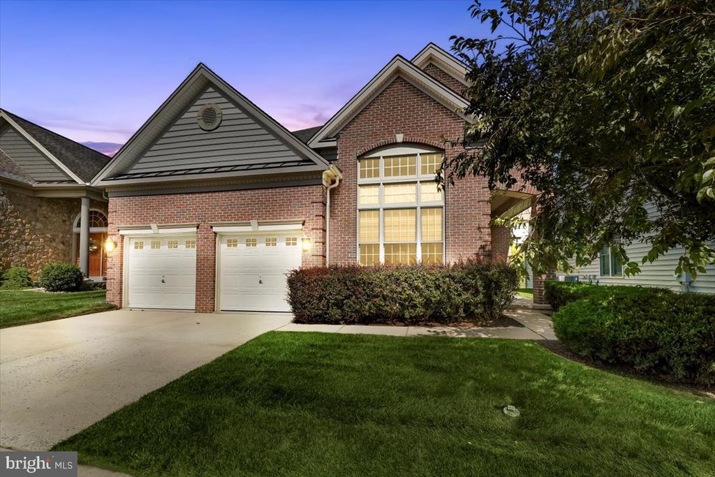 Brick home with two garage doors and a tall illuminated window at dusk.