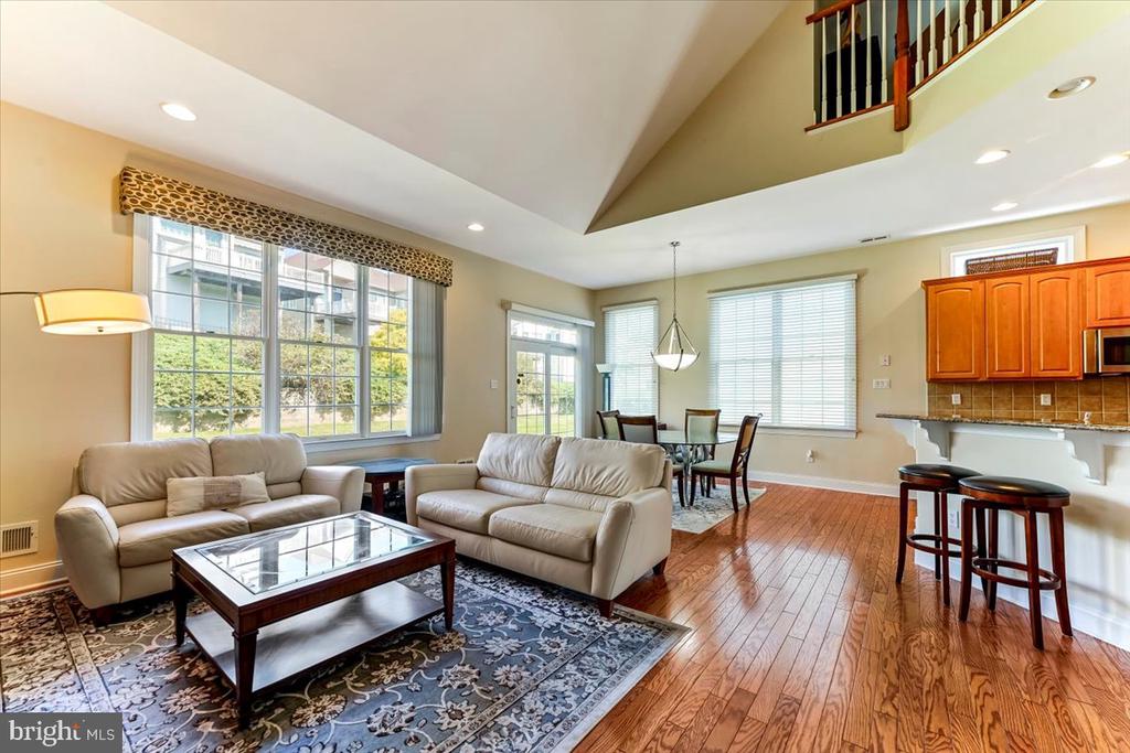 Living room with vaulted ceiling, hardwood floors, large windows, and an adjoining dining area.