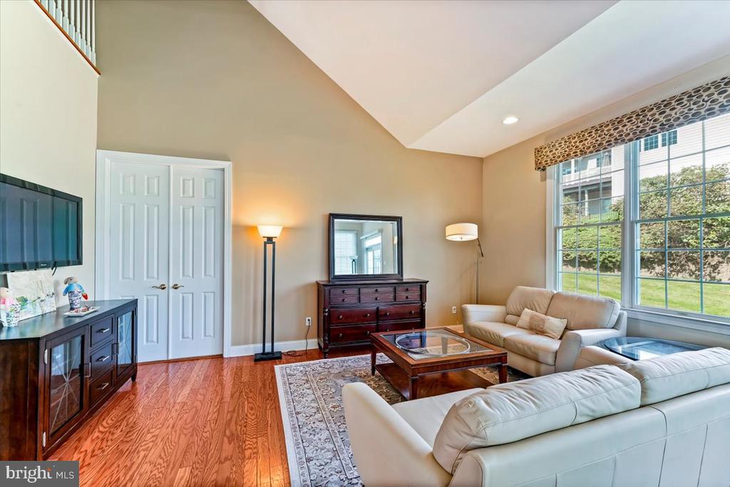 Living room with a vaulted ceiling, large yard-facing windows, hardwood floors, and a white sectional sofa.