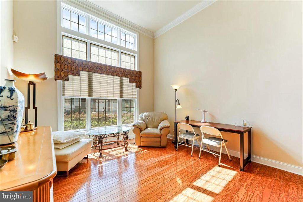 Furnished sitting area and desk beside tall windows, with glossy hardwood floors.