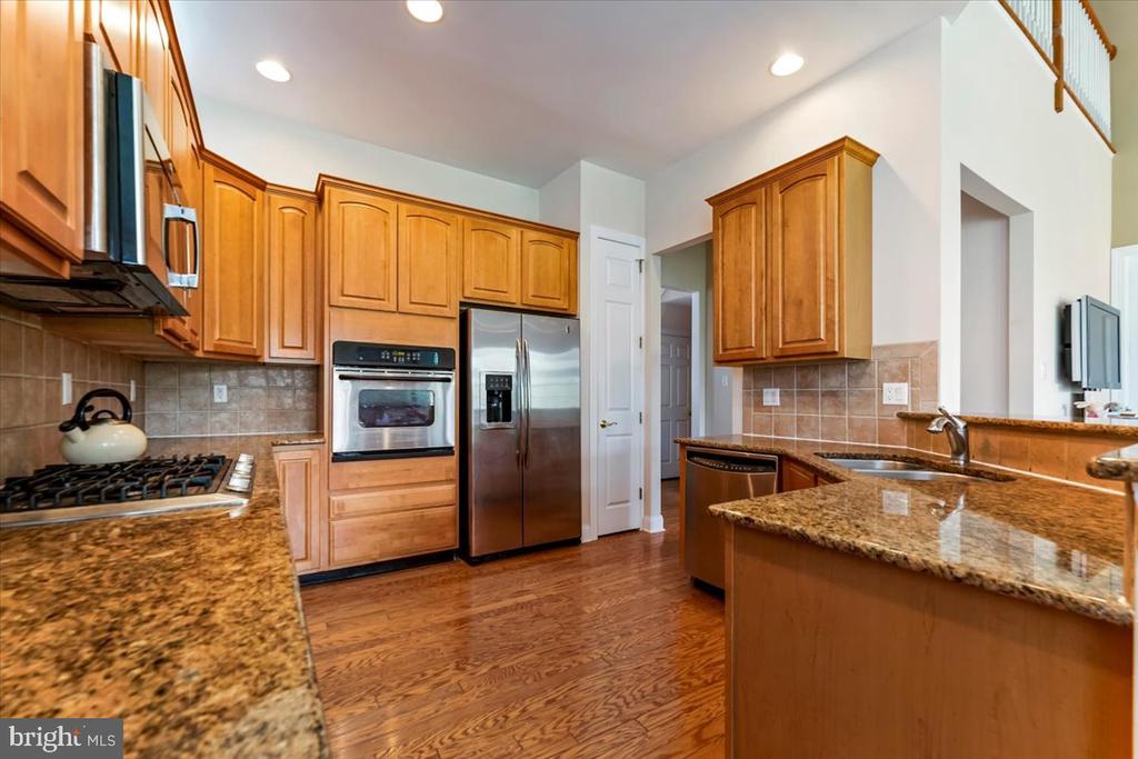 Kitchen with honey-colored cabinets, granite countertops, stainless steel appliances, and hardwood flooring.