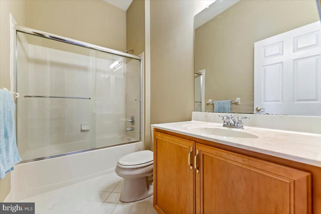 Bathroom with a glass-enclosed tub, toilet, and wood vanity with a white countertop.