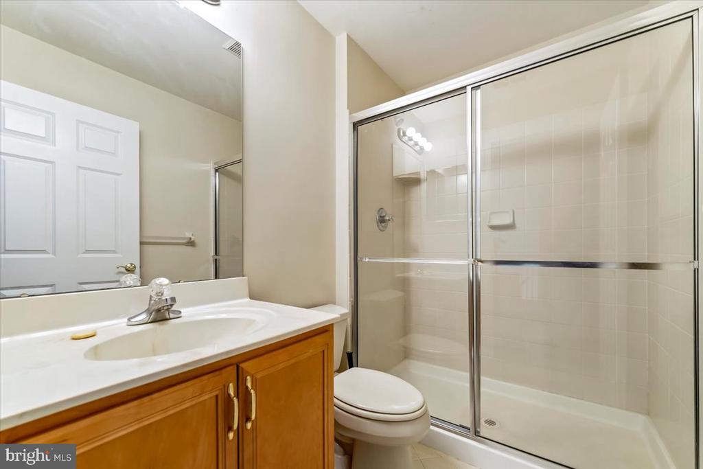 Bathroom with a wood vanity and a tiled tub-shower behind sliding glass doors.