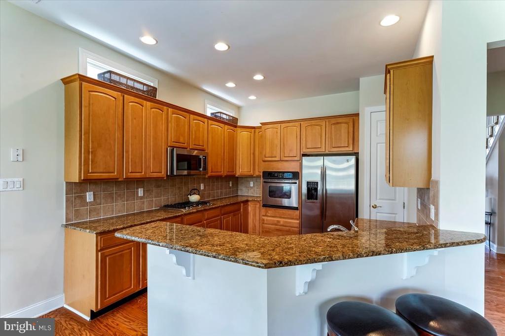 Kitchen with honey-toned cabinets, granite peninsula, bar stools, and stainless-steel appliances.