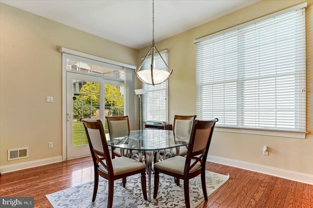 Dining room with a glass-top table, four chairs, hardwood floors, and large windows overlooking the yard.