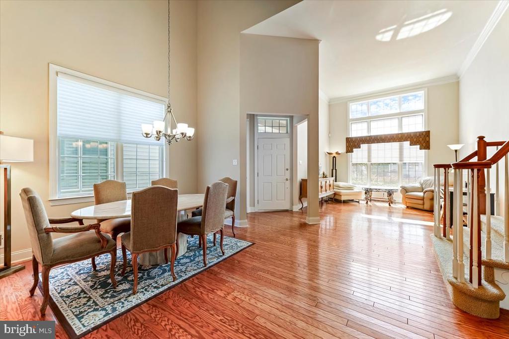 Open dining and living area with hardwood floors, large windows, and a tall ceiling.