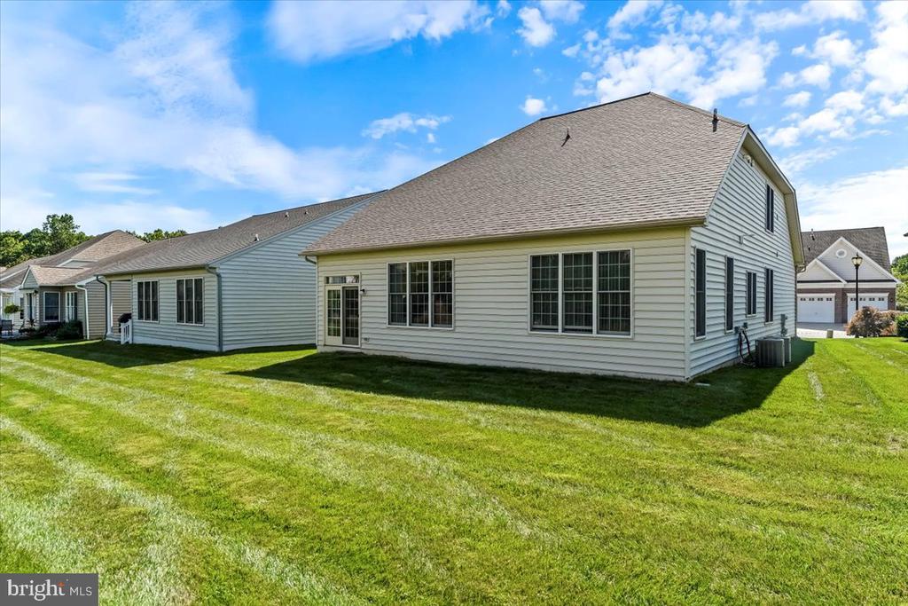 Rear and side of a light-sided home with many windows and a broad green lawn.