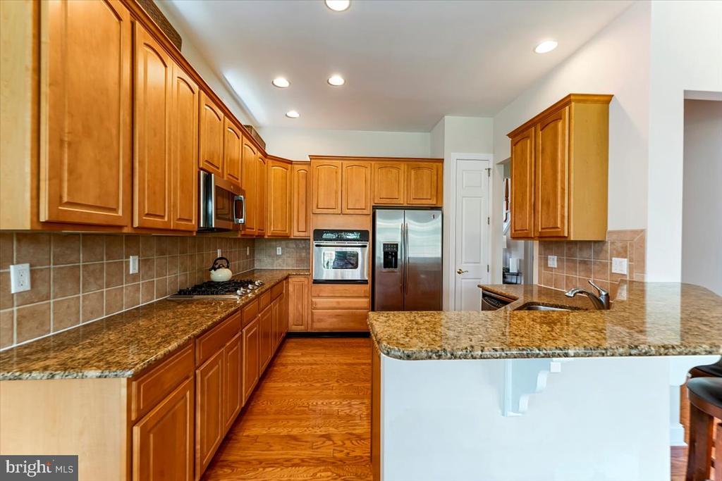 Kitchen with honey-toned wood cabinets, granite counters, stainless steel appliances, and a raised breakfast bar.