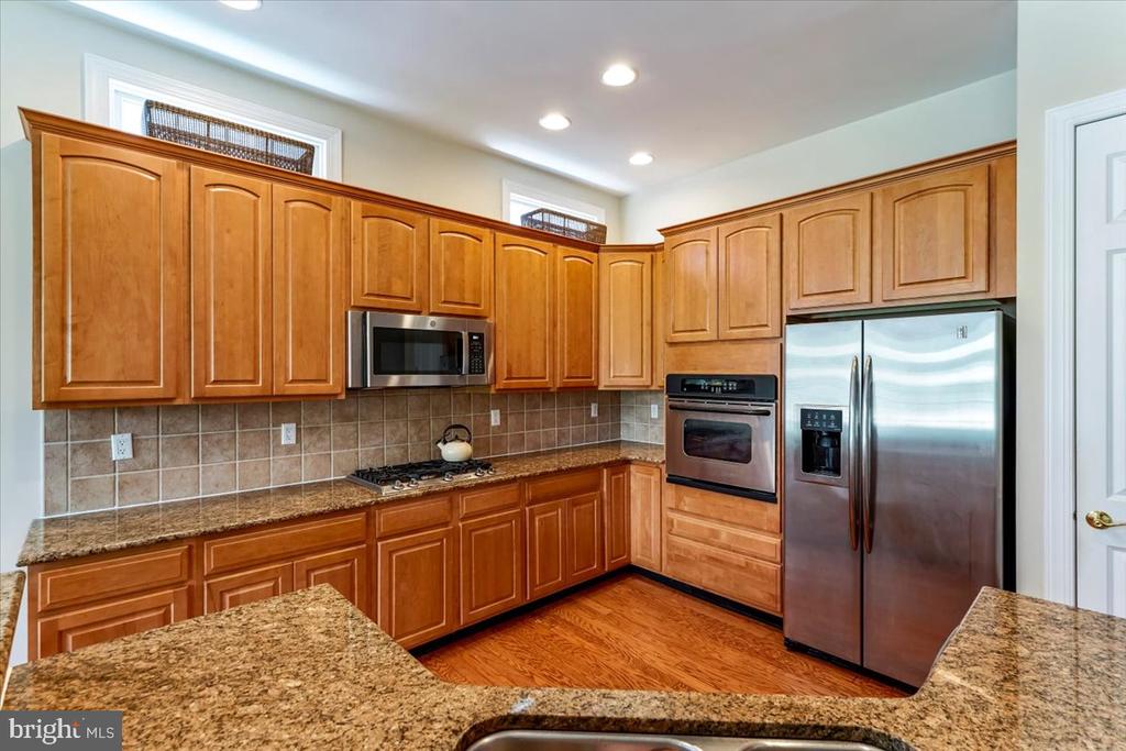 Kitchen with warm wood cabinetry, granite counters, and stainless steel appliances.