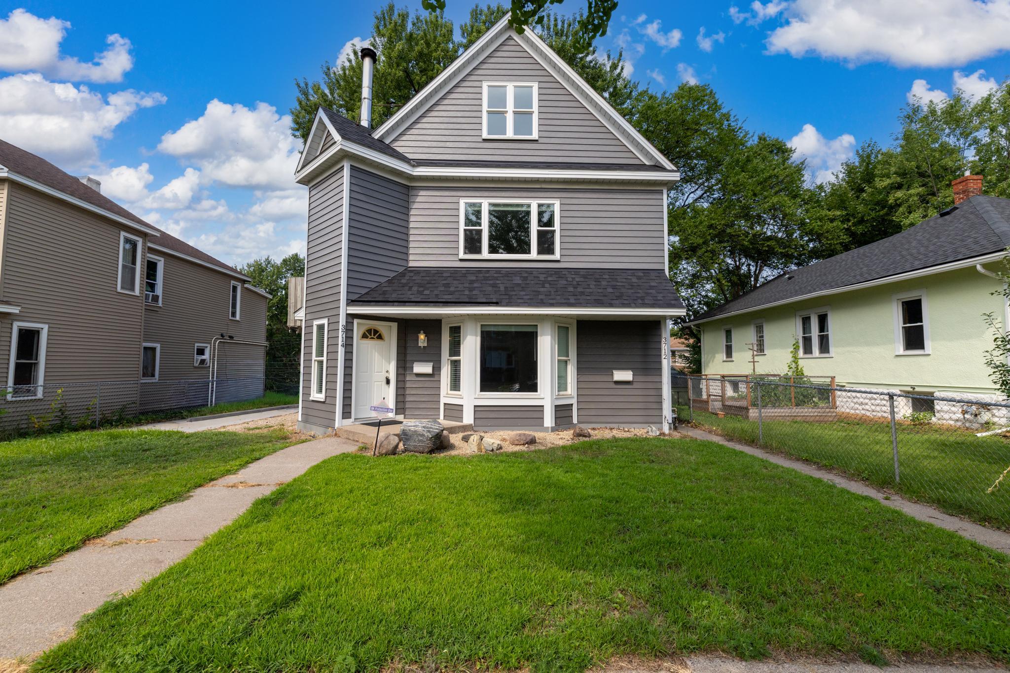 Gray three-story house with white trim, steep gable, covered entry, and green front lawn.