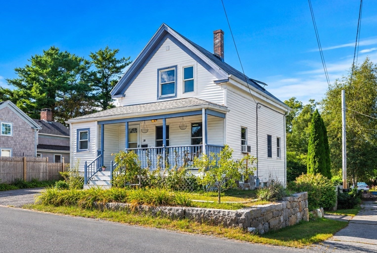 White two-story house with a blue-trimmed porch and landscaped stone-front yard.