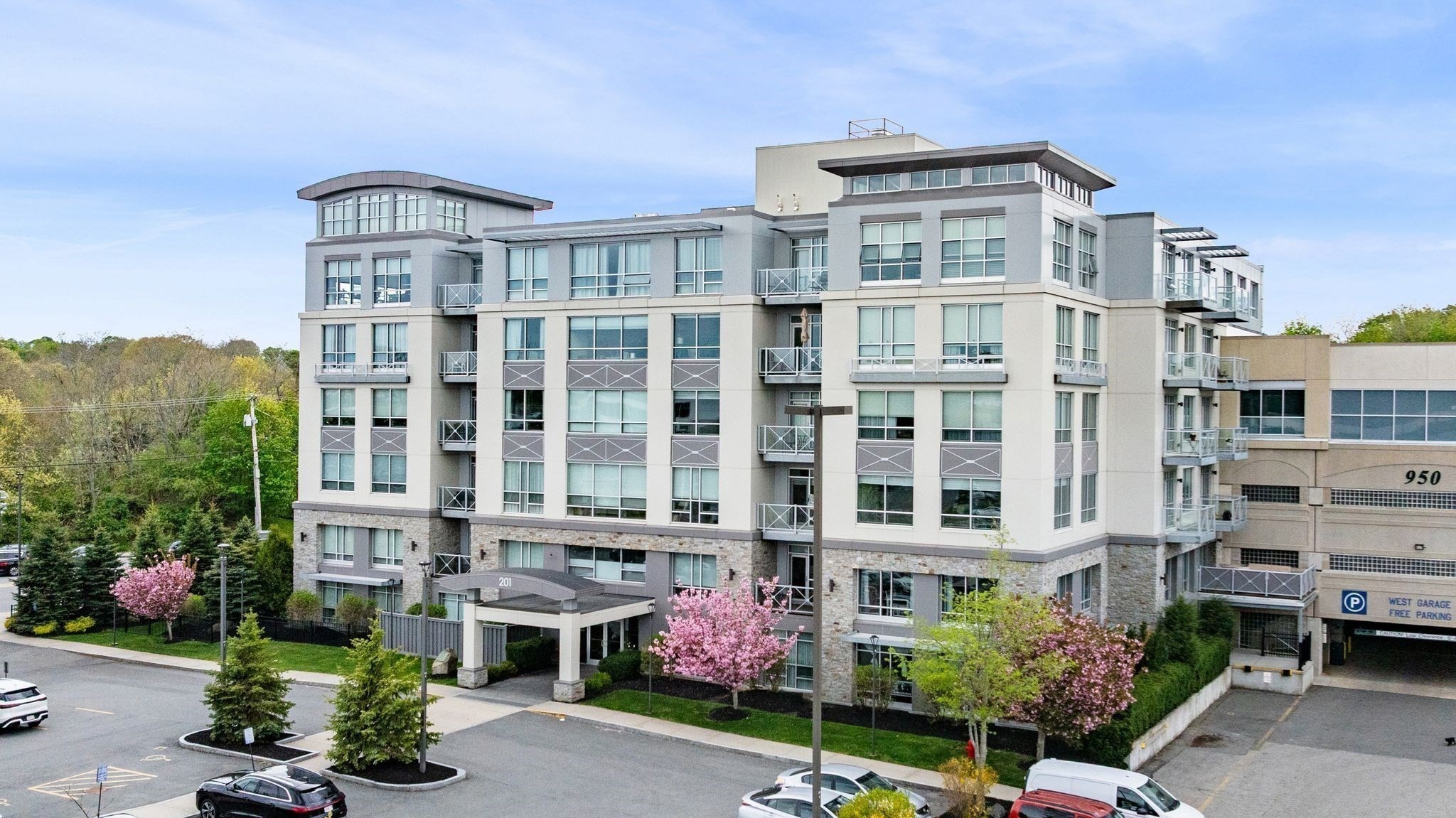 Modern multi-story condominium building with balconies, landscaped entrance, and spring blossoms.