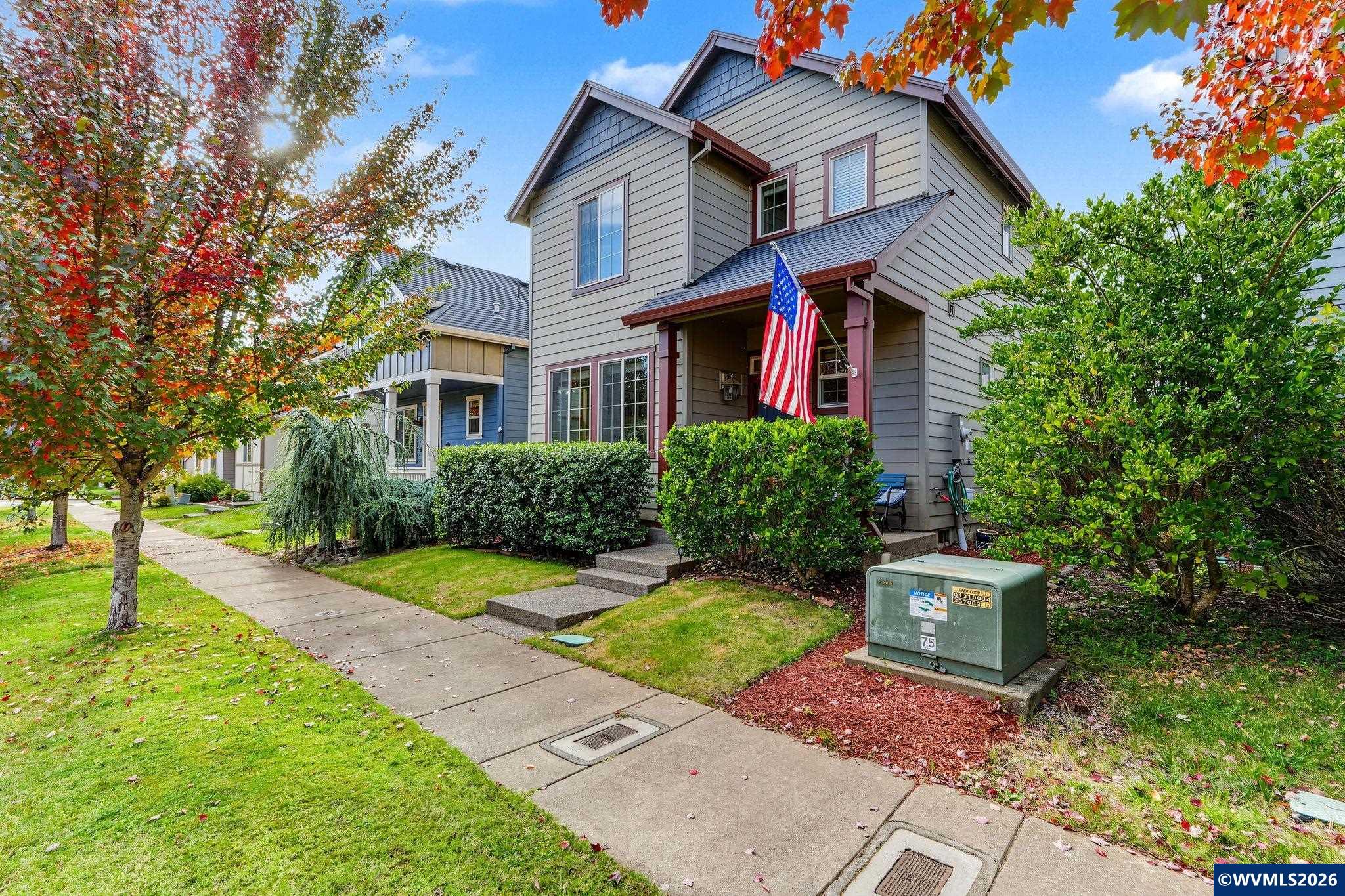 Two-story gray house with an American flag, framed by colorful autumn trees.