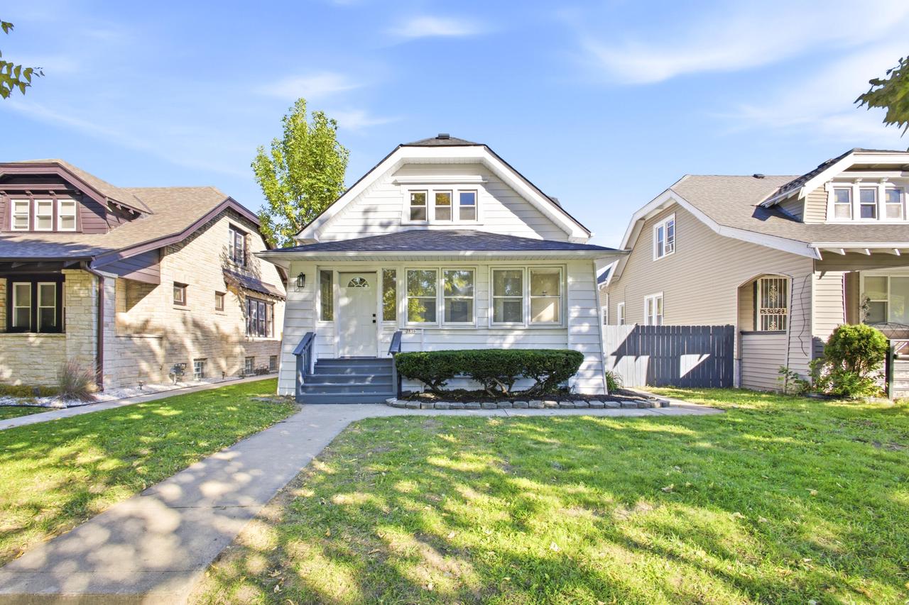 White bungalow with a broad front porch, trimmed hedge, and neighboring homes.