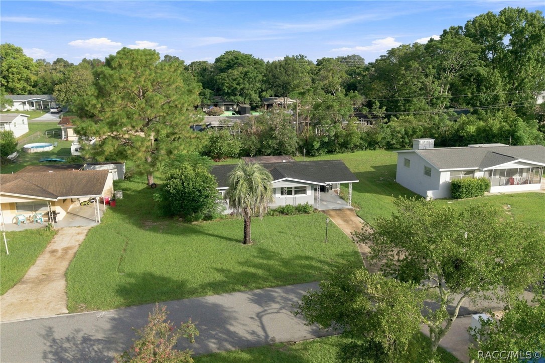 Aerial view of a single-story home with a covered carport, palm tree, and spacious lawn.