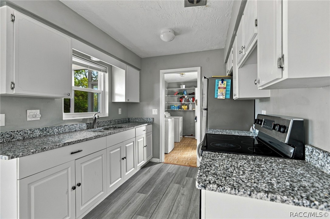 Kitchen with white cabinets, granite counters, black electric range, and a laundry area beyond the doorway.