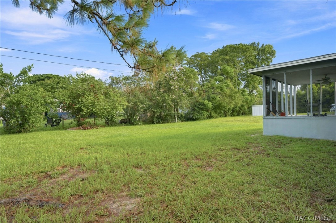 Grassy yard bordered by mature trees, with a covered porch at the right.