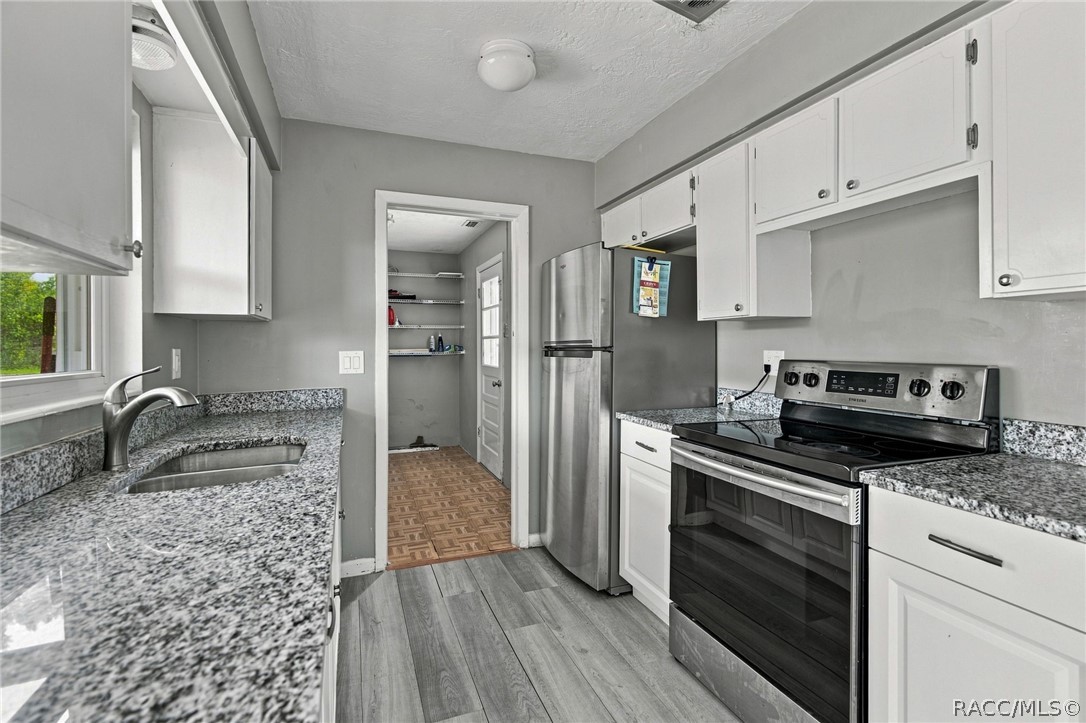 Kitchen with granite counters, white cabinets, stainless steel refrigerator, and black electric range.