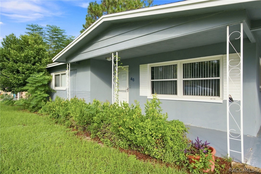 Blue-gray single-story house with a covered porch, white trim, and lush front landscaping.