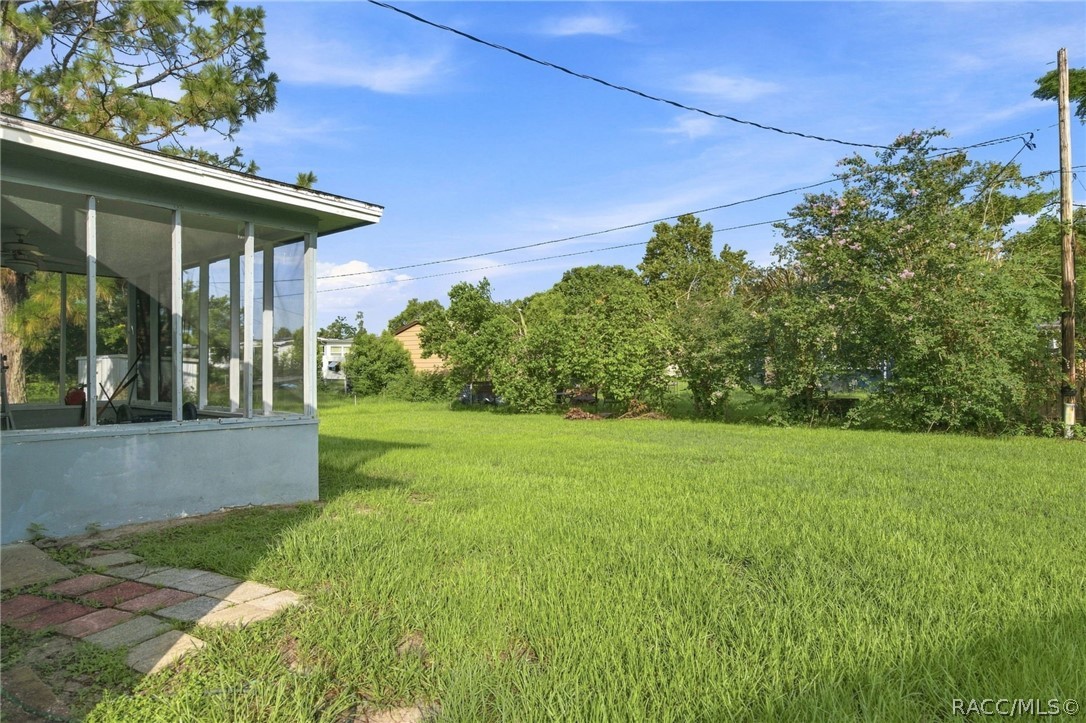 Grassy yard beside a screened porch, with mature trees and shrubs along the property edge.